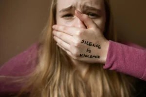 Survivor covering mouth with hand showing “Silence is Violence” written on skin, symbolic of breaking the silence around sexual assault in New Brunswick.