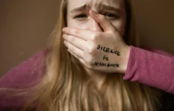 Survivor covering mouth with hand showing “Silence is Violence” written on skin, symbolic of breaking the silence around sexual assault in New Brunswick.